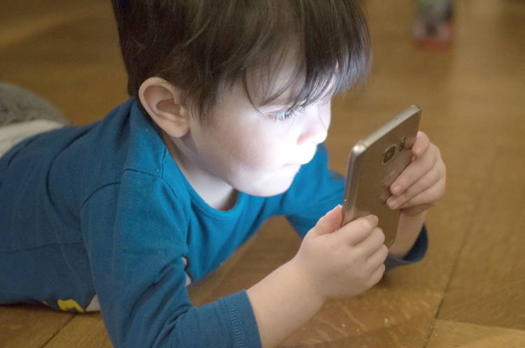 Un niño leyendo desde un móvil pegado a su cara Un niño leyendo desde un móvil pegado a su cara